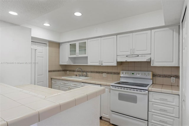 kitchen featuring a sink, tile countertops, under cabinet range hood, and white range with electric cooktop