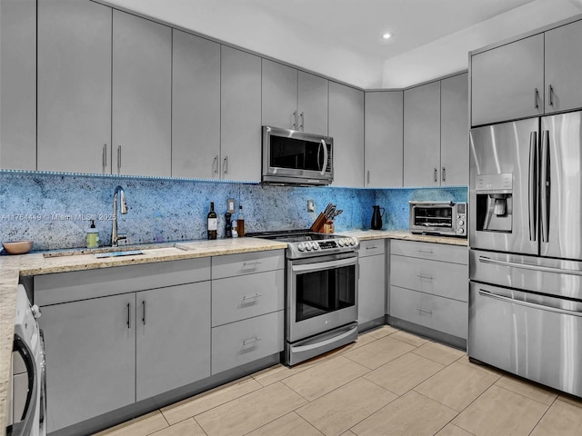 kitchen with a toaster, washer / clothes dryer, gray cabinets, a sink, and stainless steel appliances