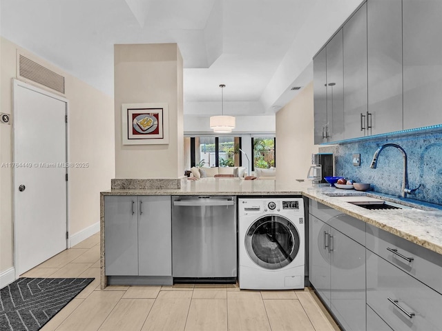 kitchen with light stone countertops, gray cabinets, stainless steel dishwasher, washer / clothes dryer, and a sink