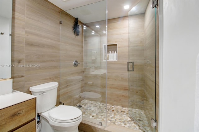 bathroom featuring tile walls, a shower stall, toilet, and vanity