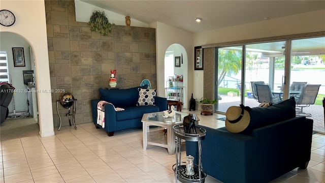 living area featuring arched walkways, light tile patterned floors, and lofted ceiling