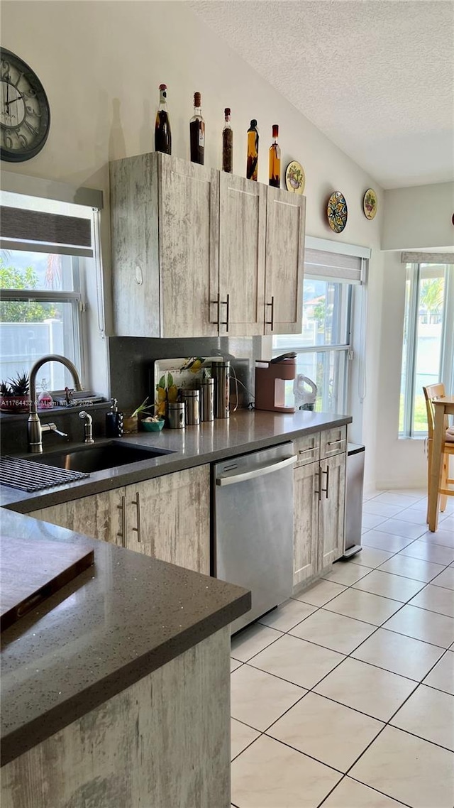 kitchen featuring light tile patterned floors, lofted ceiling, a sink, a textured ceiling, and stainless steel dishwasher