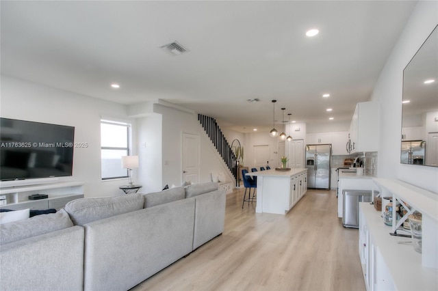 living room with recessed lighting, visible vents, stairs, and light wood finished floors