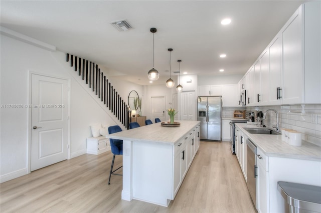 kitchen with visible vents, a breakfast bar area, light wood-style flooring, appliances with stainless steel finishes, and a sink