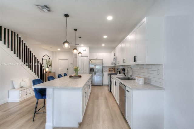 kitchen featuring visible vents, a sink, a kitchen breakfast bar, a kitchen island, and stainless steel appliances