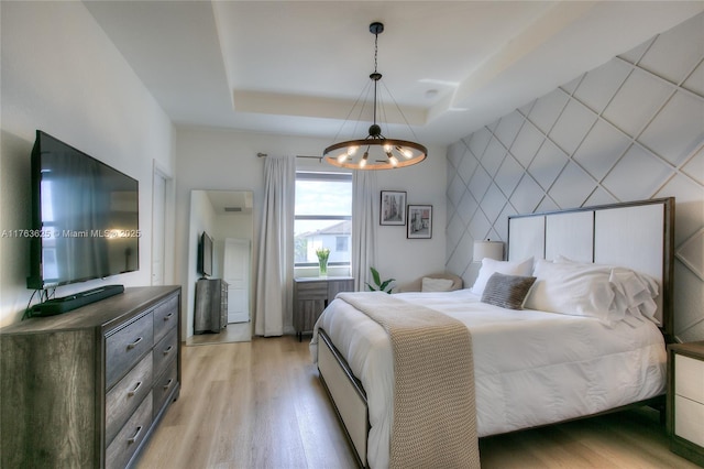 bedroom with an accent wall, a tray ceiling, a notable chandelier, and light wood-type flooring