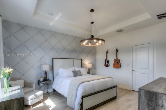 bedroom featuring visible vents, a raised ceiling, light wood-style floors, and an accent wall