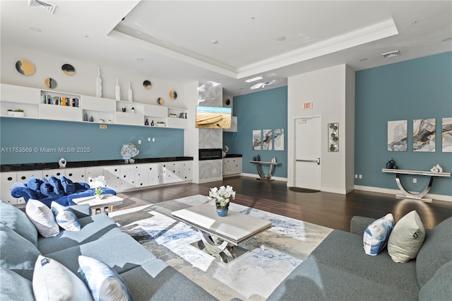 living room featuring visible vents, baseboards, a tray ceiling, and wood finished floors