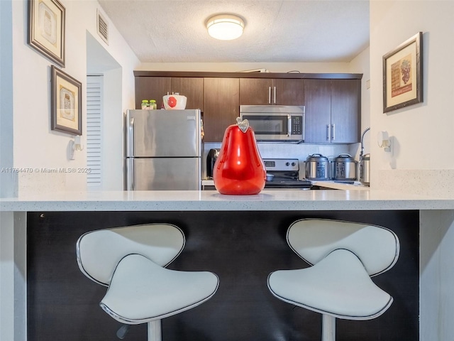 kitchen with a breakfast bar, visible vents, a peninsula, and stainless steel appliances