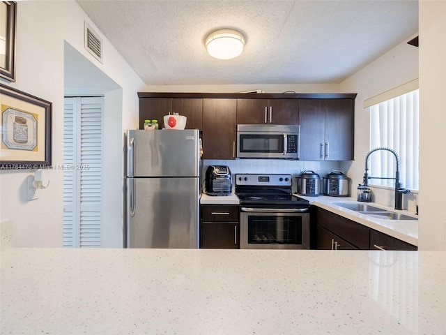 kitchen with a sink, visible vents, appliances with stainless steel finishes, and dark brown cabinets