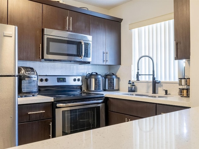 kitchen with a sink, light stone counters, tasteful backsplash, dark brown cabinetry, and appliances with stainless steel finishes