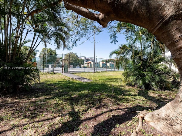 view of community featuring a gate, a tennis court, a lawn, and fence