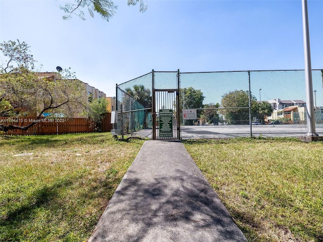 view of tennis court featuring a yard, fence, and a gate