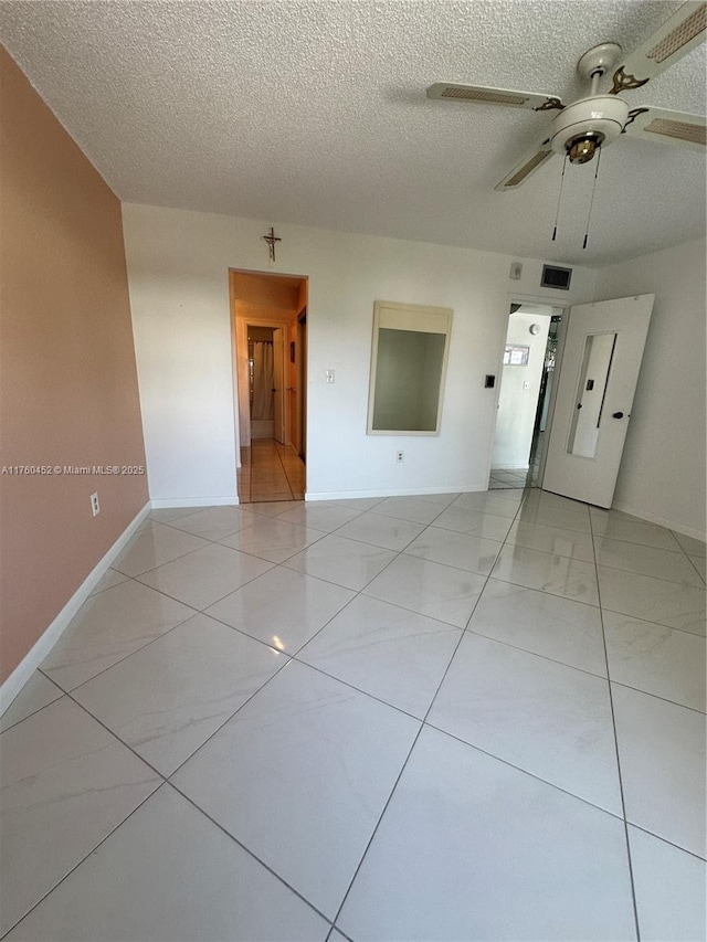 spare room with light tile patterned floors, baseboards, a textured ceiling, and a ceiling fan