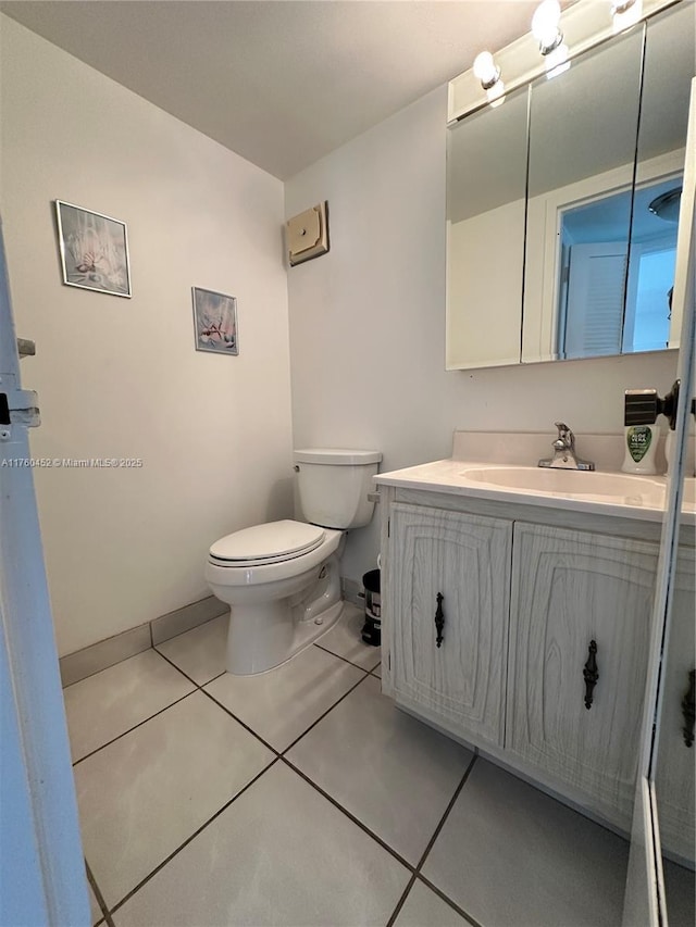 half bathroom with tile patterned flooring, toilet, vanity, and baseboards