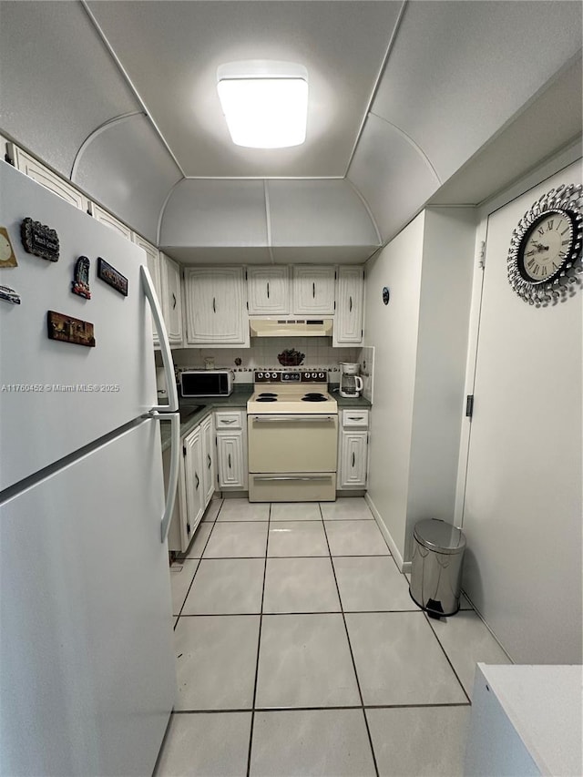 kitchen with light tile patterned floors, white appliances, under cabinet range hood, and vaulted ceiling