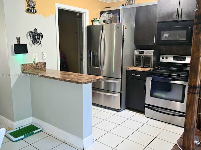 kitchen with dark cabinetry, a peninsula, appliances with stainless steel finishes, light tile patterned floors, and baseboards