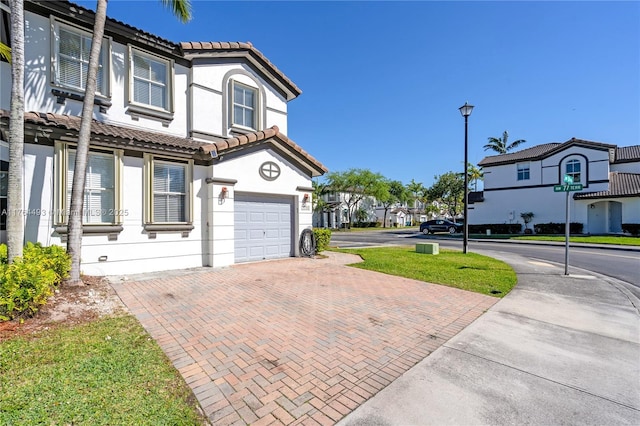 view of side of property featuring stucco siding, a tile roof, decorative driveway, a residential view, and a garage