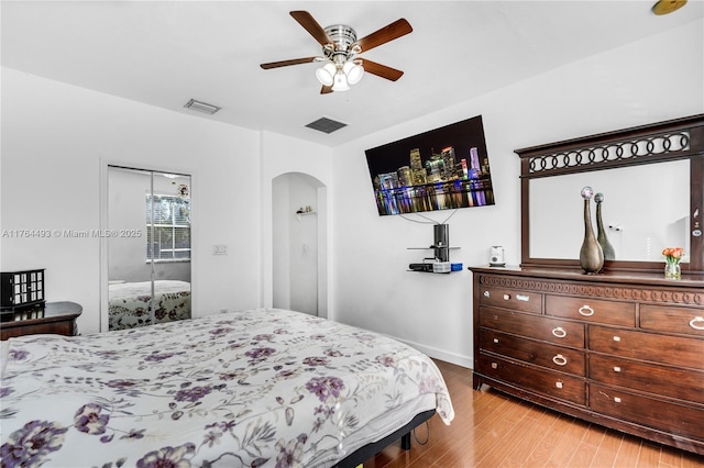 bedroom featuring light wood-style flooring, arched walkways, visible vents, and ceiling fan