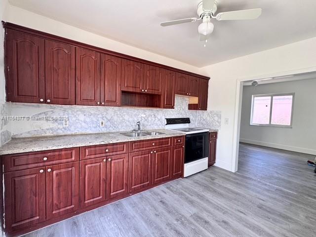 kitchen featuring electric range, light wood-style flooring, a sink, backsplash, and reddish brown cabinets