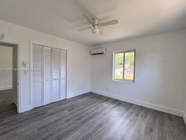 unfurnished bedroom featuring dark wood-type flooring, a wall unit AC, baseboards, and a closet