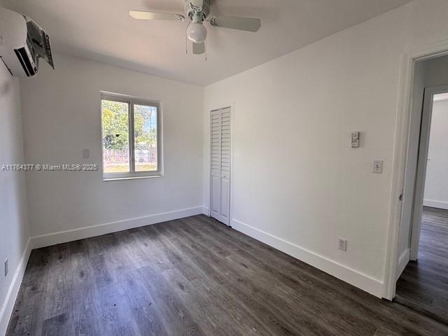 spare room with dark wood-type flooring, a wall unit AC, a ceiling fan, and baseboards