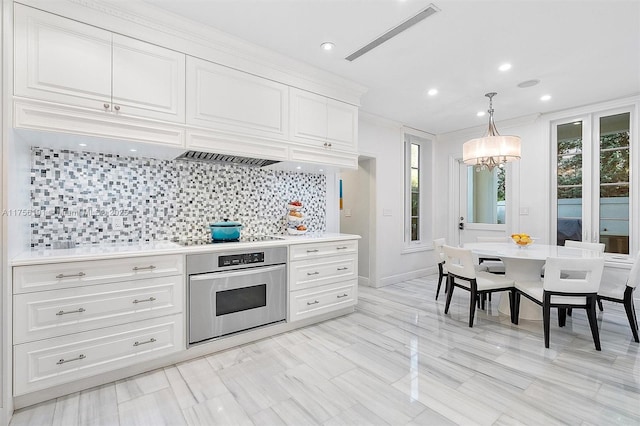 kitchen with black electric stovetop, stainless steel oven, decorative backsplash, a notable chandelier, and white cabinets