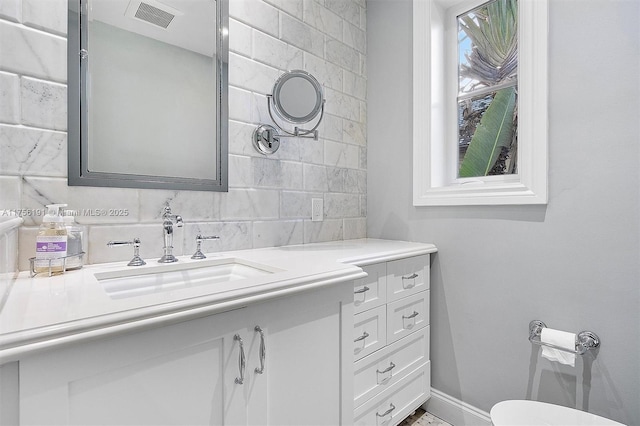 half bath with tasteful backsplash, visible vents, baseboards, toilet, and vanity