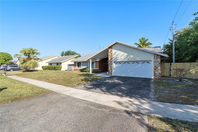 view of front of property with a front lawn, fence, driveway, stone siding, and an attached garage