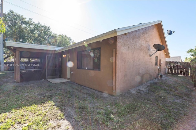 view of side of property with stucco siding, a sunroom, and fence