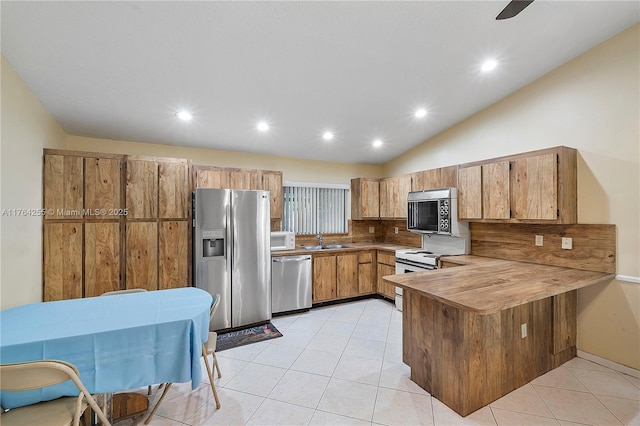 kitchen featuring a sink, stainless steel appliances, a peninsula, light tile patterned flooring, and decorative backsplash