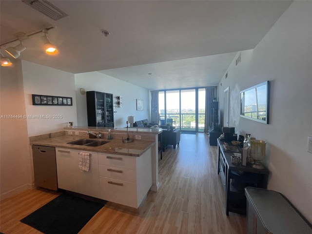 kitchen with light wood finished floors, a peninsula, a sink, white cabinets, and dishwasher