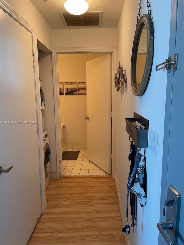 hall featuring light wood-style flooring, stacked washer / drying machine, and visible vents