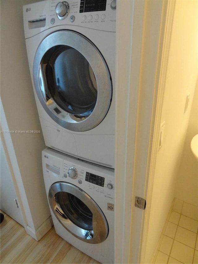 clothes washing area with laundry area, light wood-style flooring, baseboards, and stacked washing maching and dryer