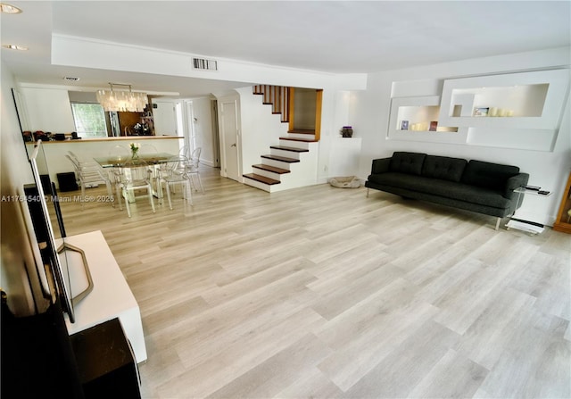 living room with visible vents, light wood-style flooring, stairway, and an inviting chandelier