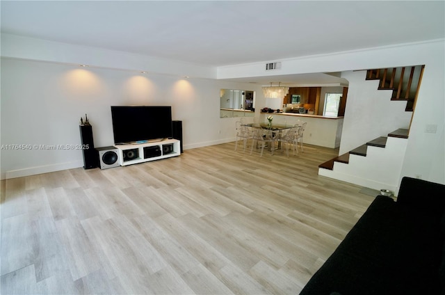 living room with light wood-type flooring, visible vents, baseboards, a chandelier, and stairs