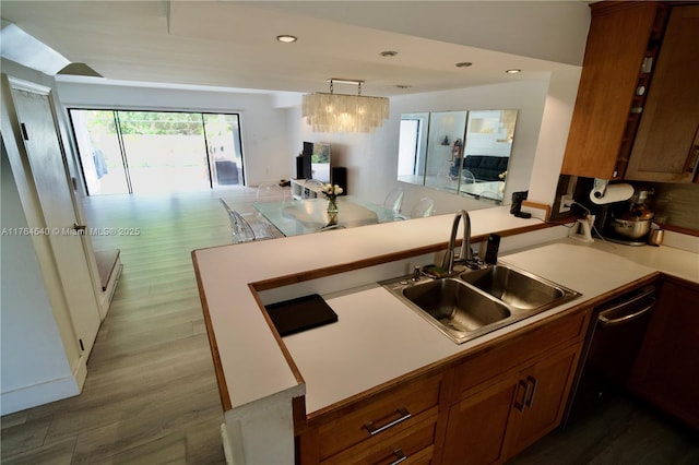 kitchen with dishwasher, brown cabinets, a peninsula, wood finished floors, and a sink