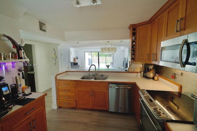 kitchen with brown cabinets, a peninsula, stainless steel appliances, and a sink