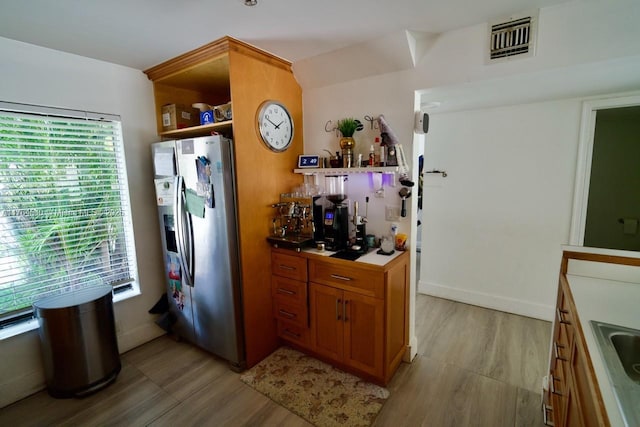 kitchen featuring visible vents, open shelves, a sink, brown cabinetry, and stainless steel fridge with ice dispenser