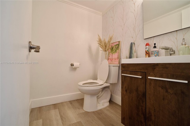 half bath featuring vanity, wood finished floors, baseboards, crown molding, and toilet