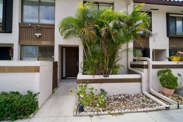 entrance to property featuring stucco siding and fence