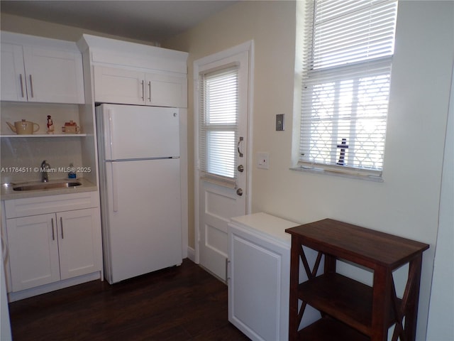 kitchen featuring dark wood finished floors, white cabinets, freestanding refrigerator, and a sink