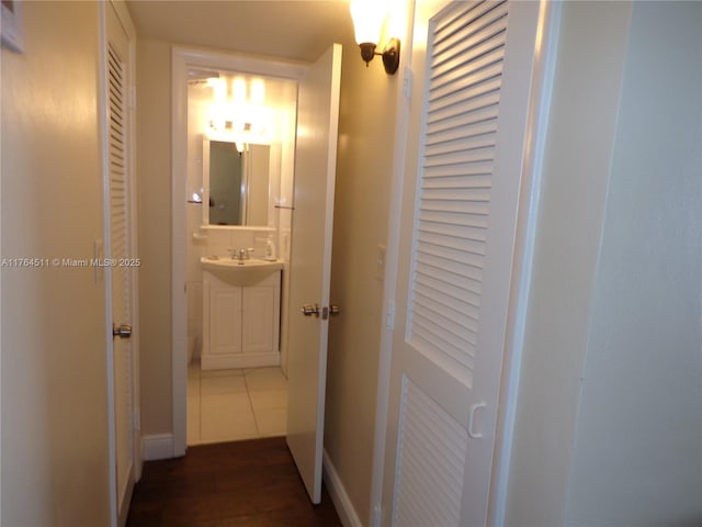 corridor featuring tile patterned floors, baseboards, and a sink