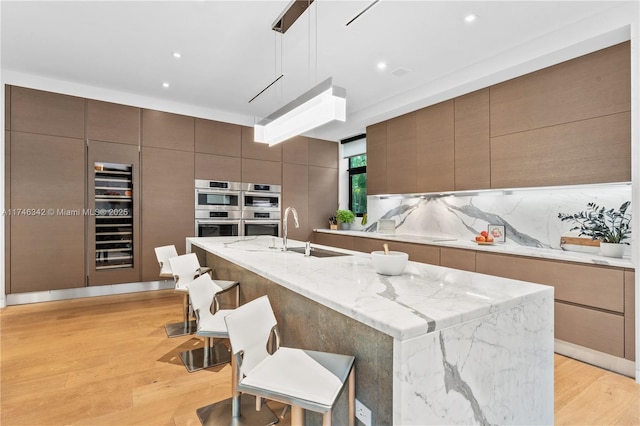 kitchen with tasteful backsplash, light wood-style flooring, double oven, and a sink