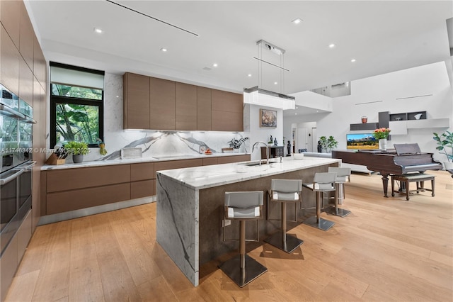 kitchen with modern cabinets, a kitchen island with sink, light wood-style flooring, a sink, and a breakfast bar area