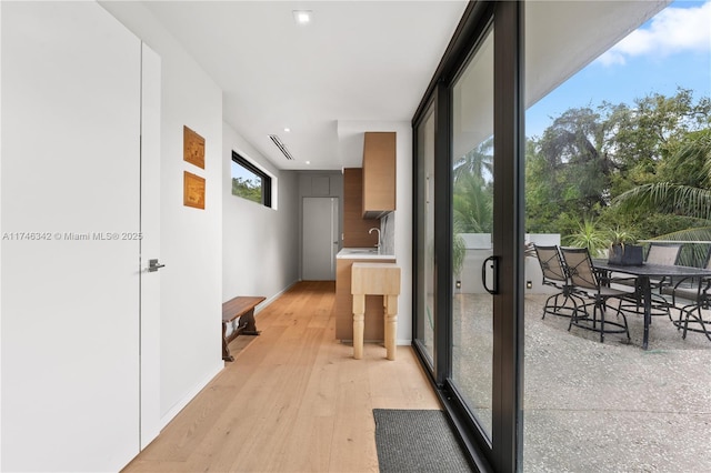 corridor featuring floor to ceiling windows, baseboards, light wood finished floors, and a sink