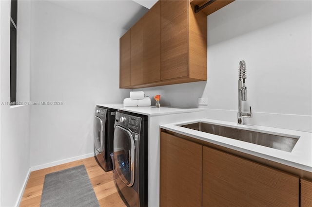 laundry area featuring light wood-type flooring, washer and dryer, a sink, cabinet space, and baseboards