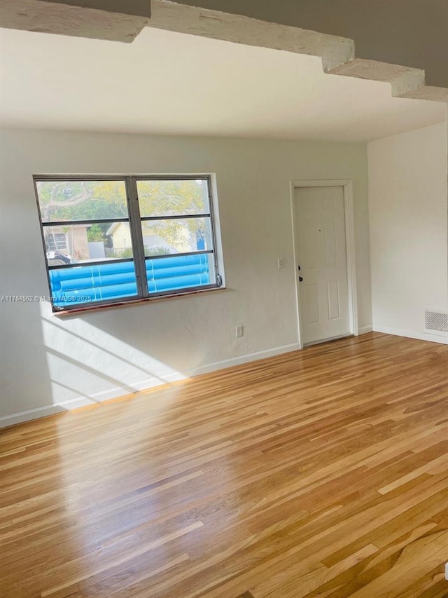 spare room with wood finished floors, visible vents, and baseboards