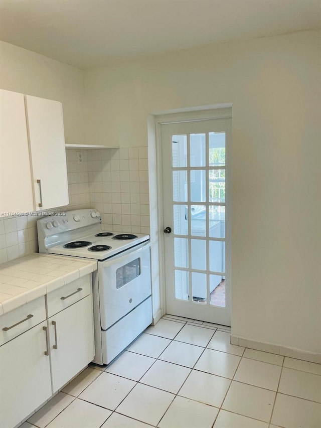 kitchen with backsplash, tile countertops, light tile patterned floors, electric stove, and white cabinets