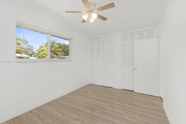 unfurnished bedroom with light wood-style flooring, a ceiling fan, baseboards, and multiple closets